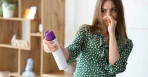 A woman pinching her nose in disgust as she holds an unlabeled can of aerosolized odor spray inside her home.