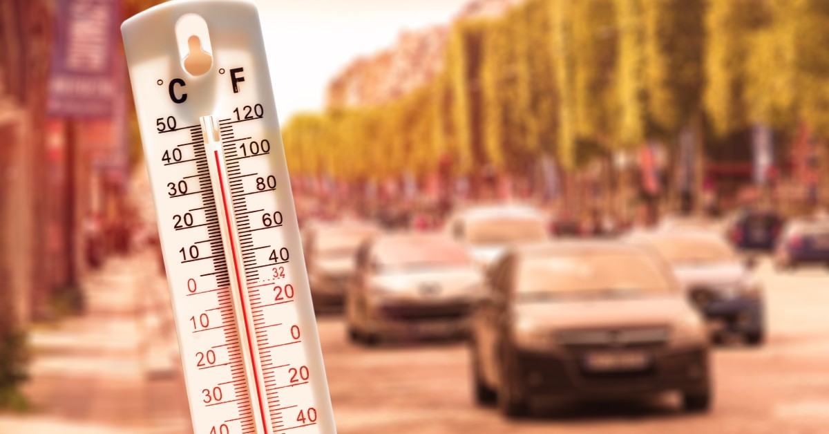 A thermometer displayed in front of moving cars showing a temperature of over 100 degrees Fahrenheit.