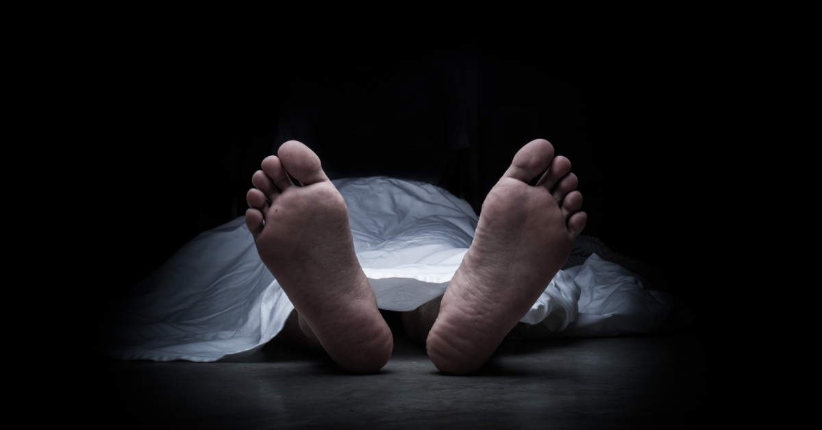 A body on the ground with a white sheet covering everything except the feet. The surroundings are pitch black.