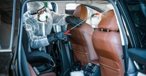 A person inside of a vehicle spraying the back of the passenger seat. The person is wearing protective clothing.