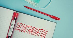 A close-up of a notebook labeled "decontamination" in all capital letters with a red pen, mask, and blood vial next to it.