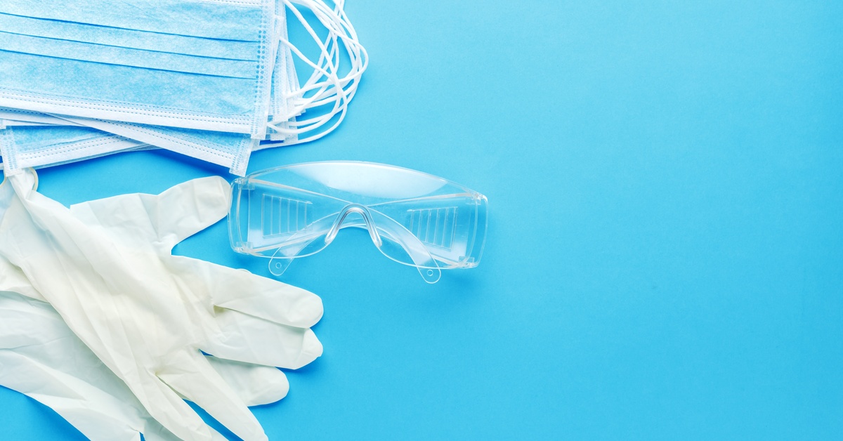 Protective glasses, alongside gloves and disposable masks sitting in piles against a blue background.