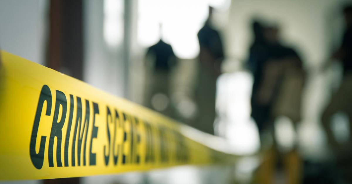 A close-up of a yellow crime scene tape, blurring as it stretches into a hallway with vague shapes of people standing.