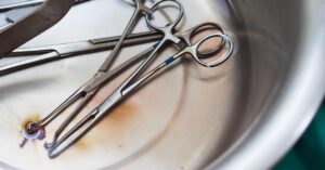 A close-up of metal surgical instruments, including forceps and clamps, in a stainless steel dish.