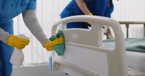 A close-up of two people wearing protective gloves cleaning a bed with side bumpers with disinfecting sprays.
