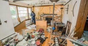 A room filled with clutter during a remodel or cleanout. A person wearing a protective mask stands in the back.