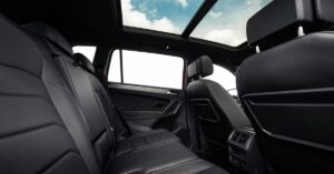 A rear row of black leather car seats beneath a panoramic roof in a clean vehicle interior with open windows.