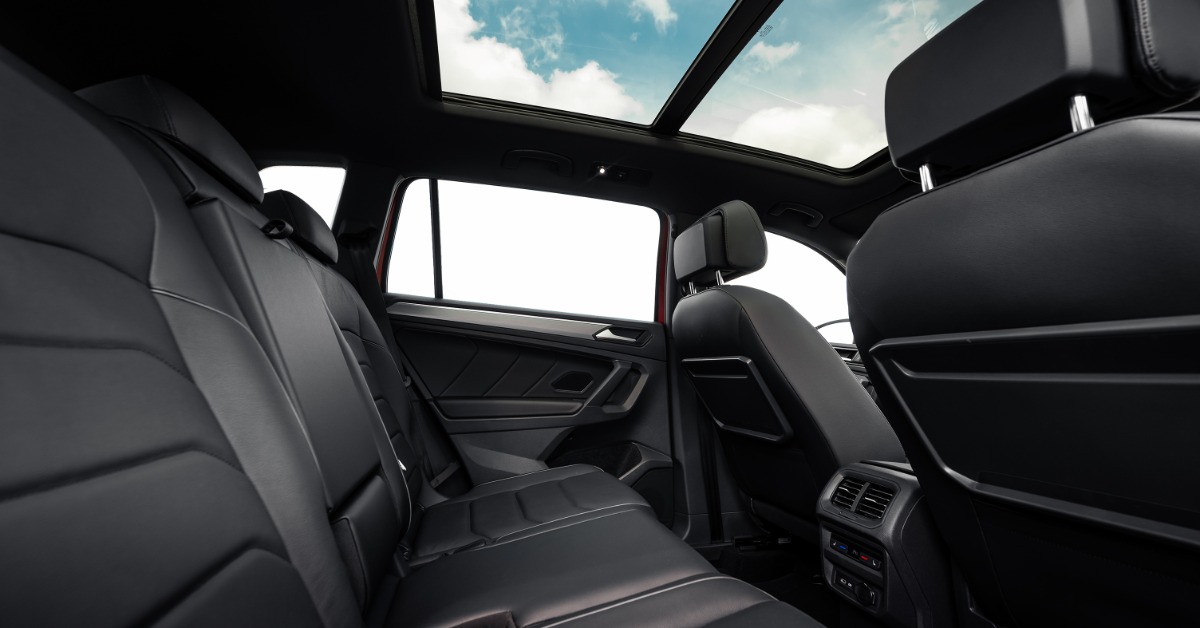 A rear row of black leather car seats beneath a panoramic roof in a clean vehicle interior with open windows.